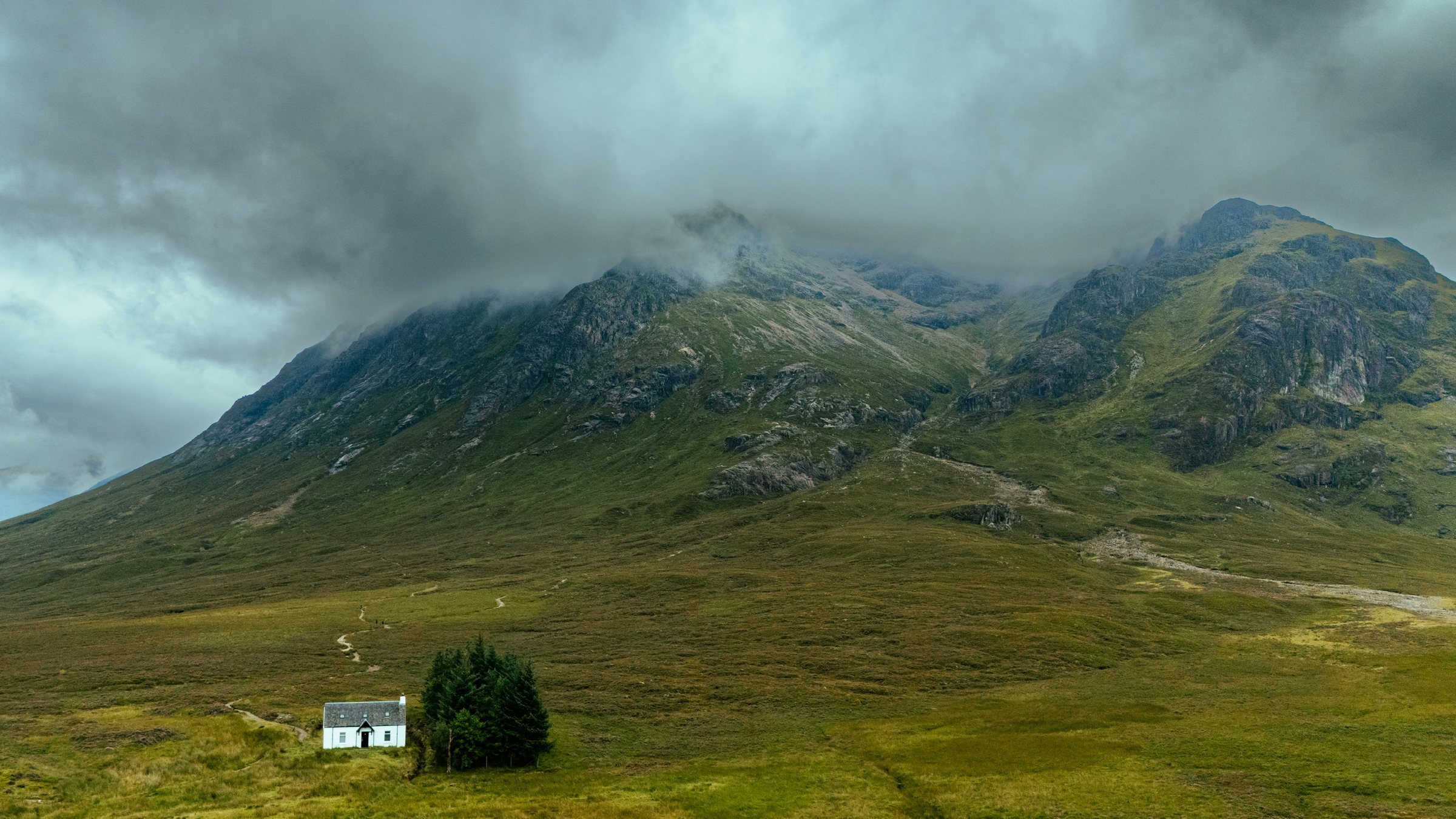 A white cottage beneath cloud-capped mountains in the Scottish Highlands